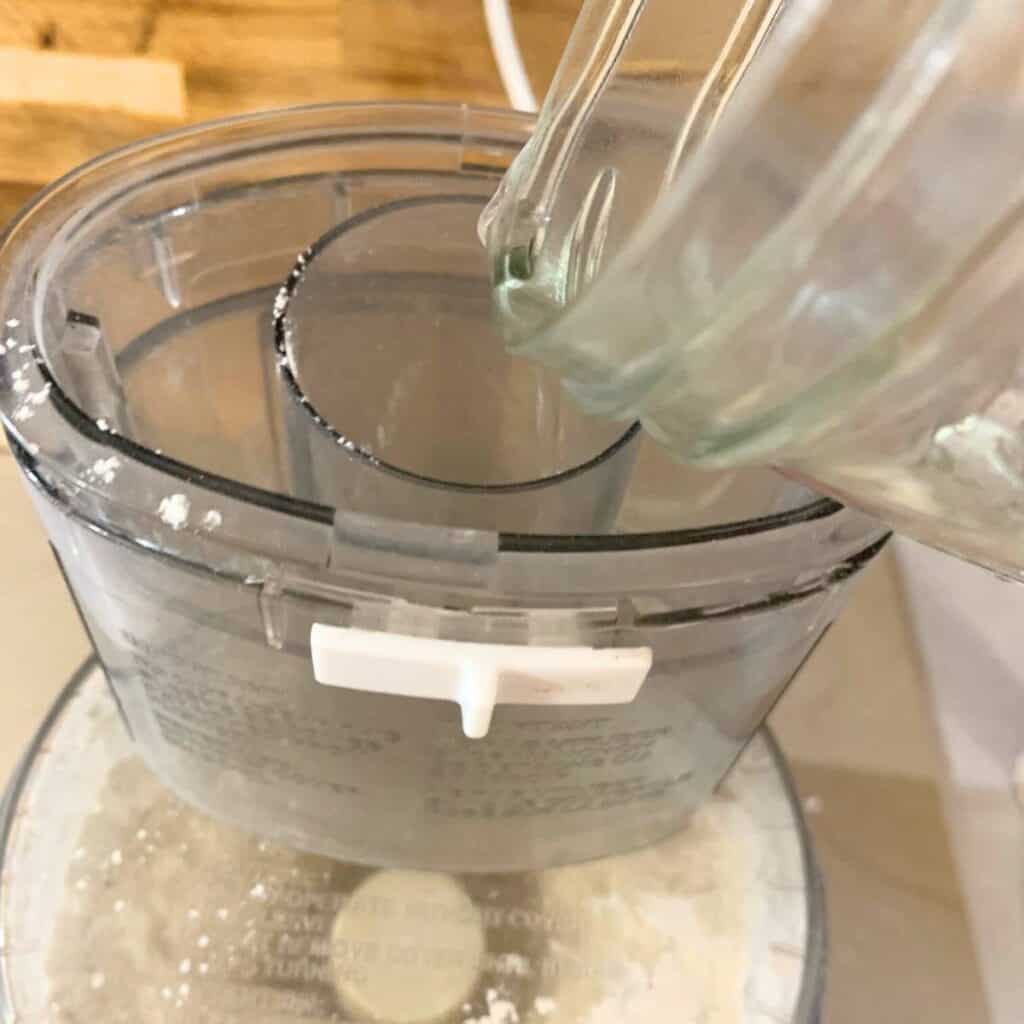 Woman adding water to a food processor to make 3 ingredient biscuits without milk.