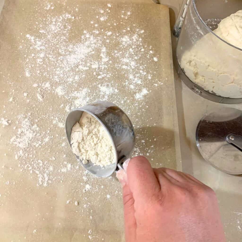 Woman sprinkling flour onto a cookie sheet lined with parchment paper.