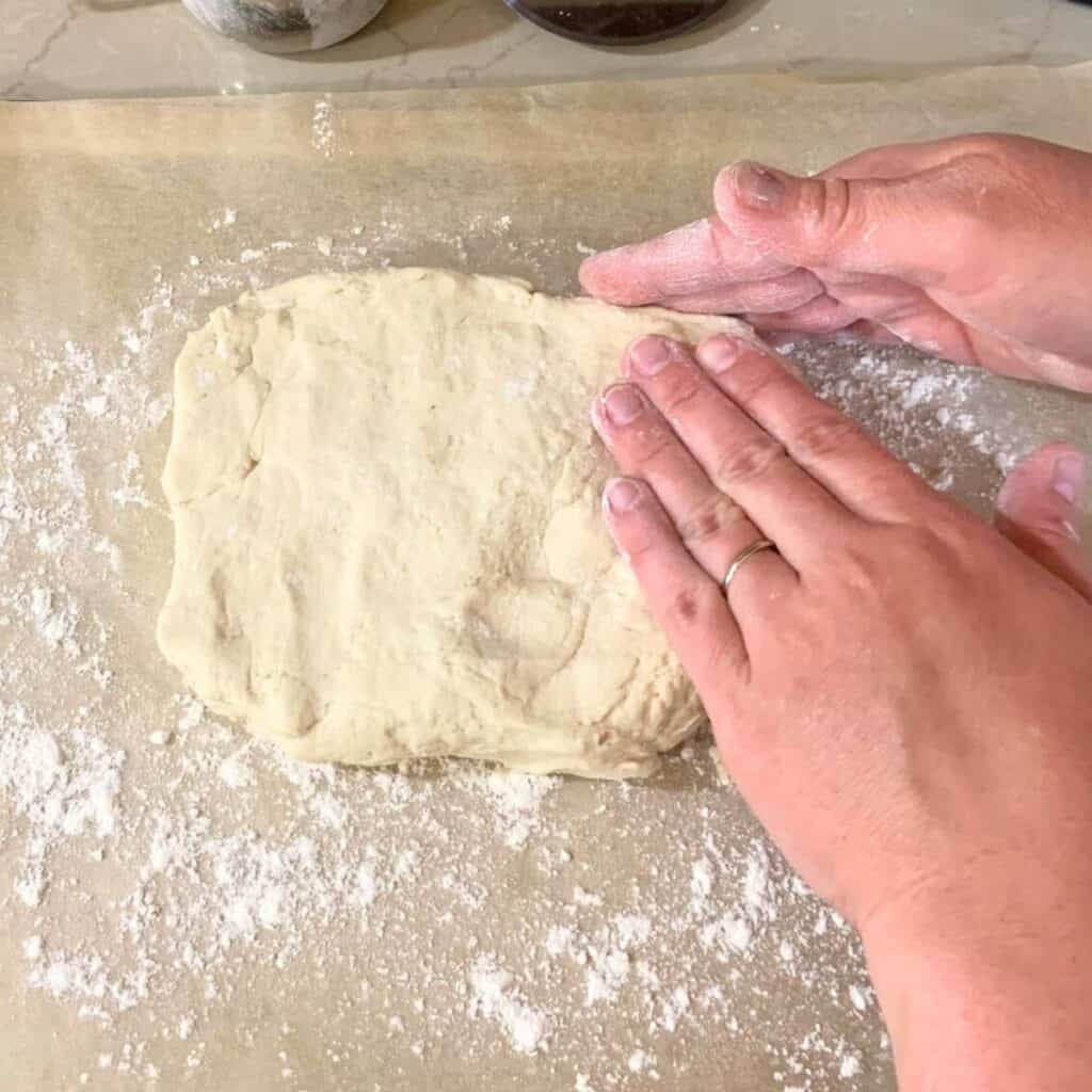 Woman spreading out biscuit dough with her hands.