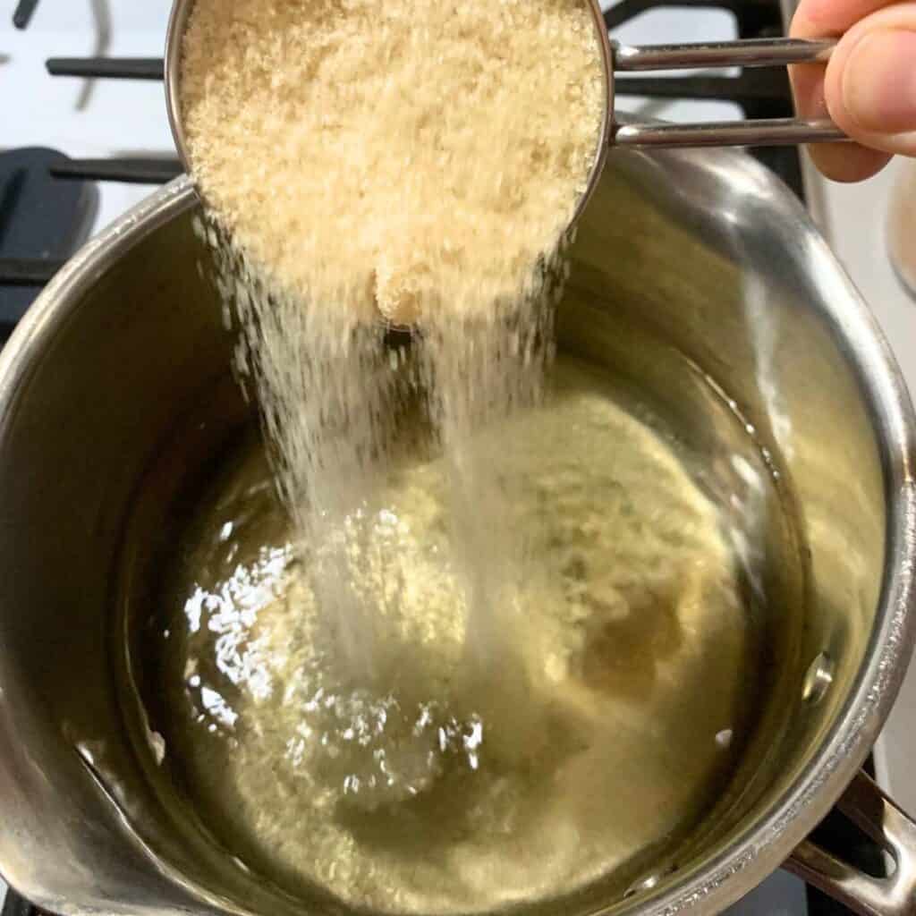 Woman adding sugar to a medium pot of water on the stove.