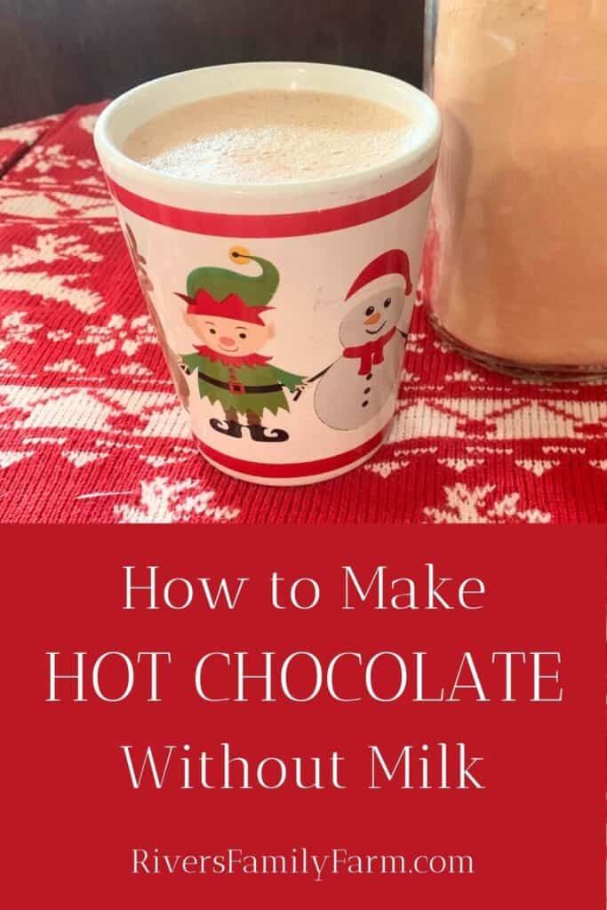 A white mug with a red stripe and an elf and penguin holding hands is sitting on a table covered with a red and white tablecloth. The mug has frothy hot chocolate inside. A glass jar of powdered cocoa mix sits behind the mug. The title is "How to Make Hot Chocolate Without Milk" by Rivers Family Farm.