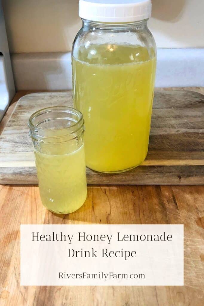 A glass of healthy honey lemonade sitting on a wooden cutting board in front of a half-gallon mason jar of lemonade. The title is "Healthy Honey Lemonade Drink Recipe" by Rivers Family Farm.