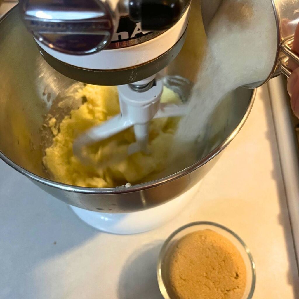 Woman adding sugar to a stand mixer with butter inside.