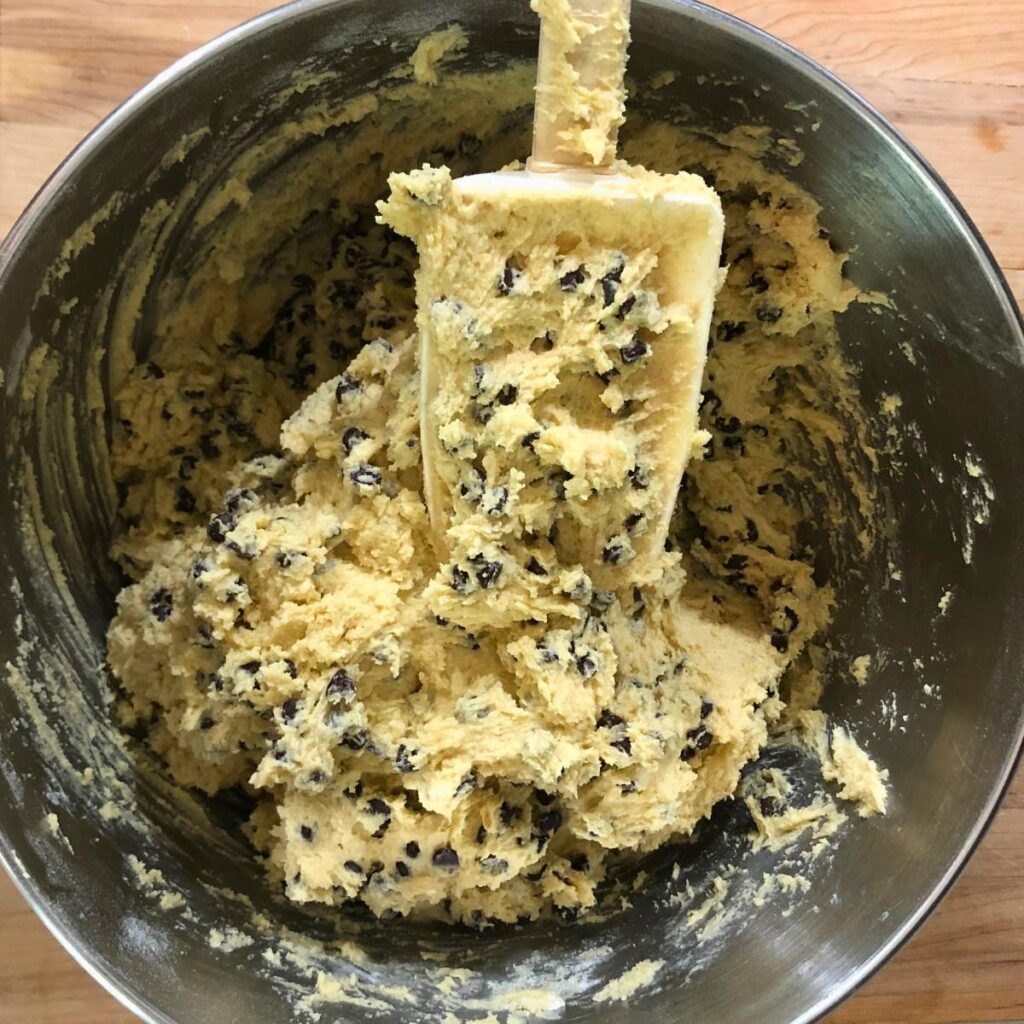 Woman stirring chocolate chips into chocolate chip cookie dough.