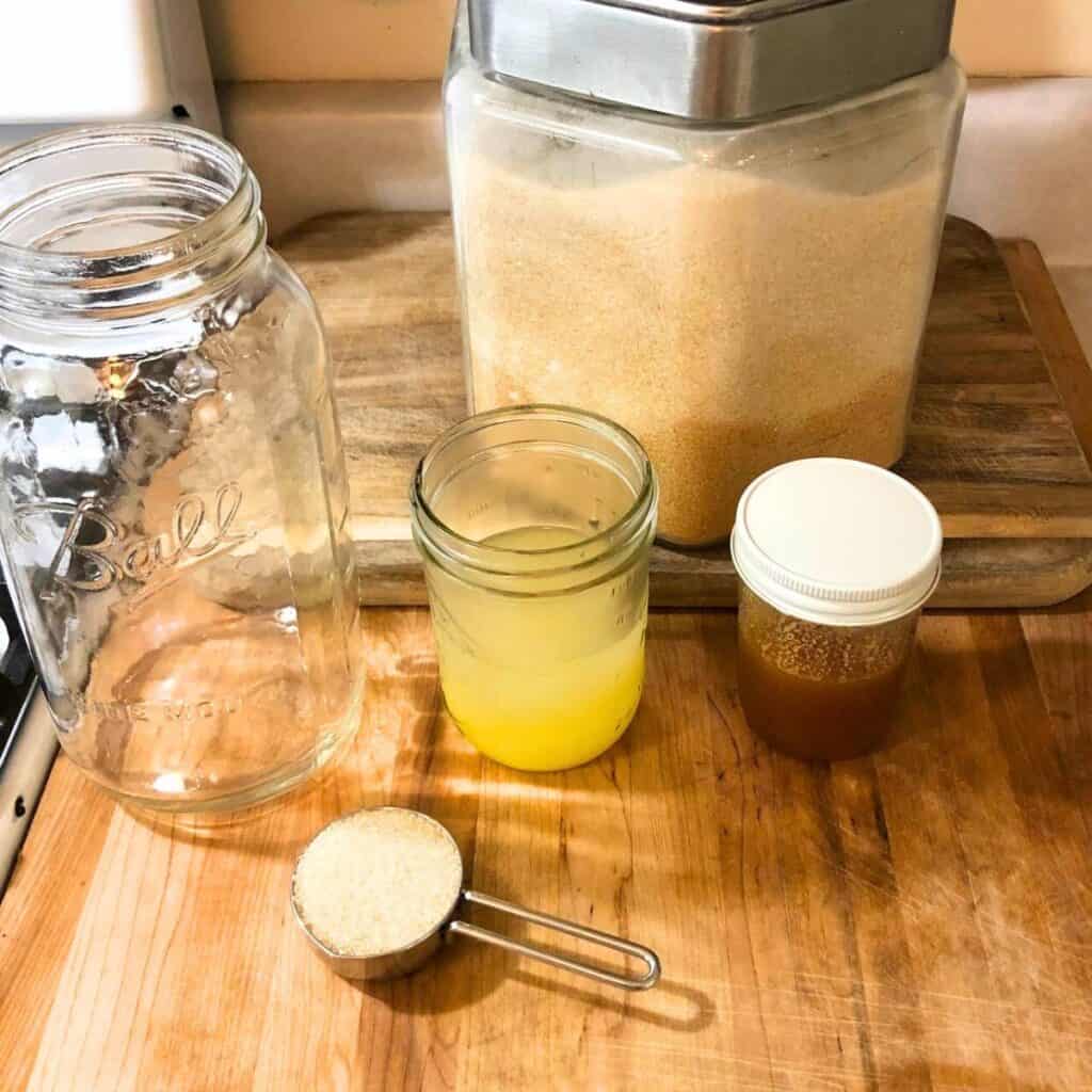 Ingredients to make lemonade including lemon juice, sugar, and honey, sitting on a wooden cutting board.