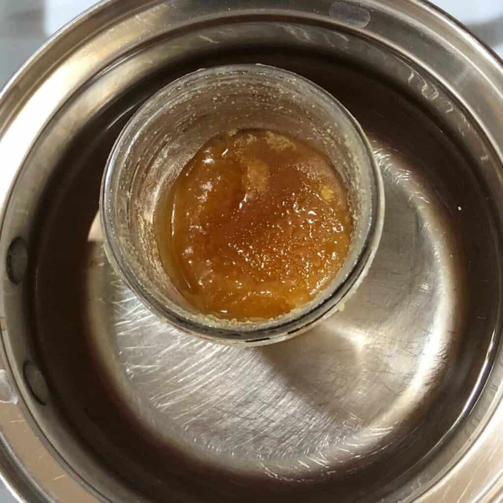 Crystallized honey in a glass pint jar sitting in a small pot with an inch of water.