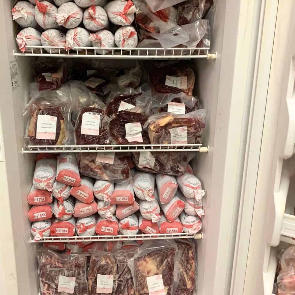 A white upright freezer filled with packaged frozen beef cuts.