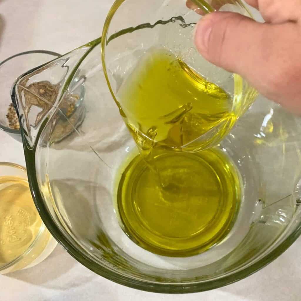 Woman pouring oil in a large glass measuring cup.