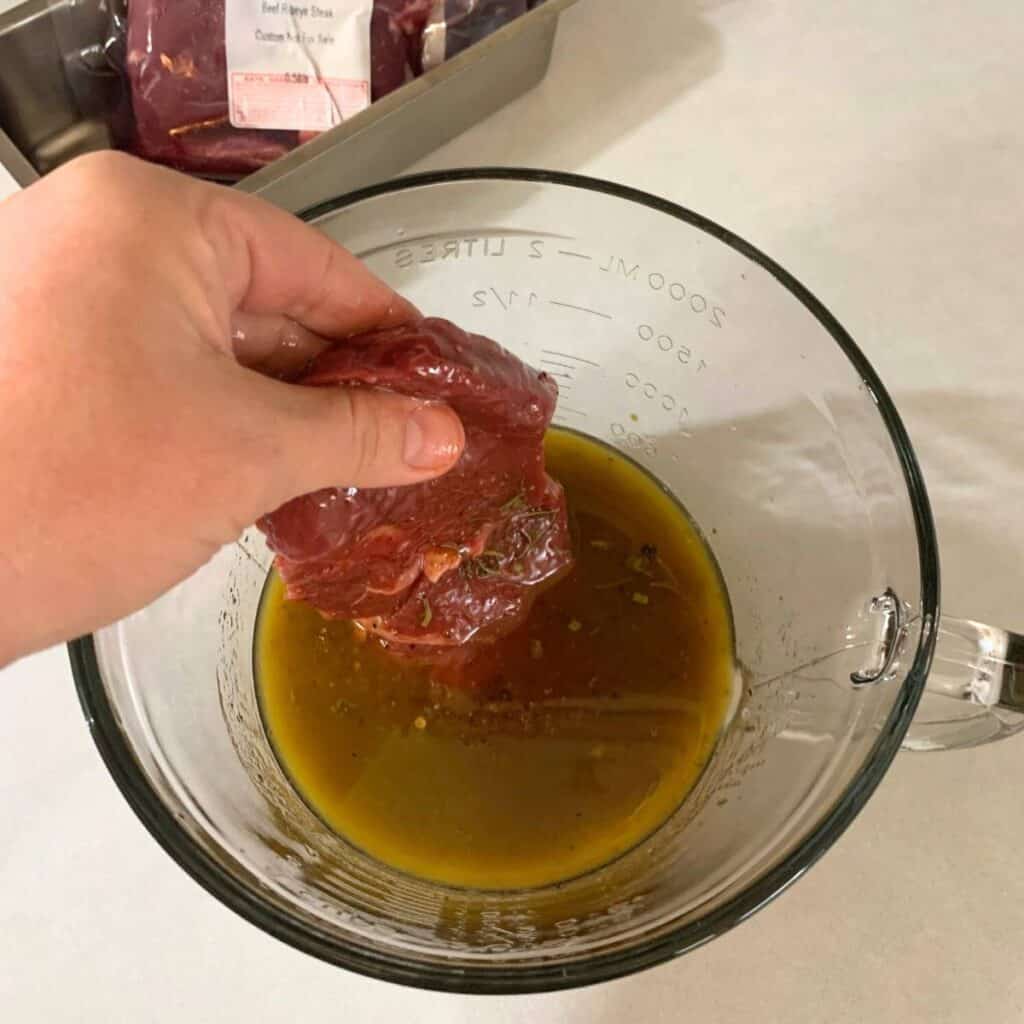 Woman putting steak into large glass measuring cup along with homemade steak marinade.