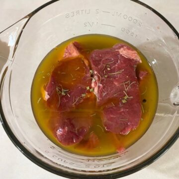 Steaks submerged in a large glass measuring cup of homemade steak marinade.