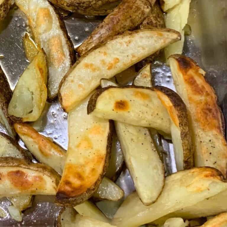 Baked wedge fries in a shallow stainless steel roasting pan.