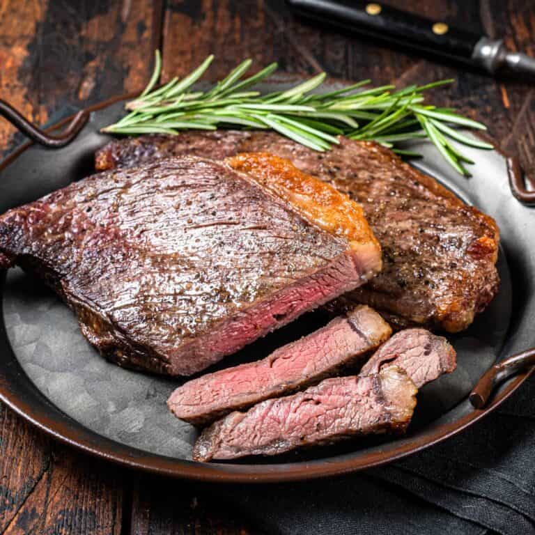 A sirloin tip roast on a plate with a sprig of rosemary.