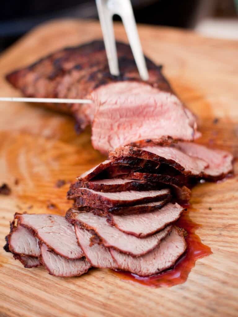 Woman slicing a sirloin tip roast on a wood cutting board.