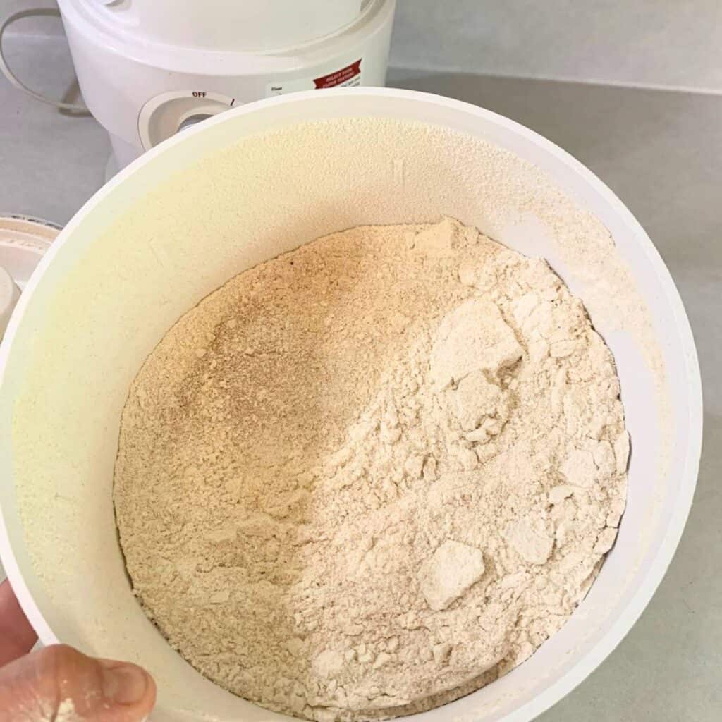 A woman holding a white bowl filled with freshly milled whole wheat flour.