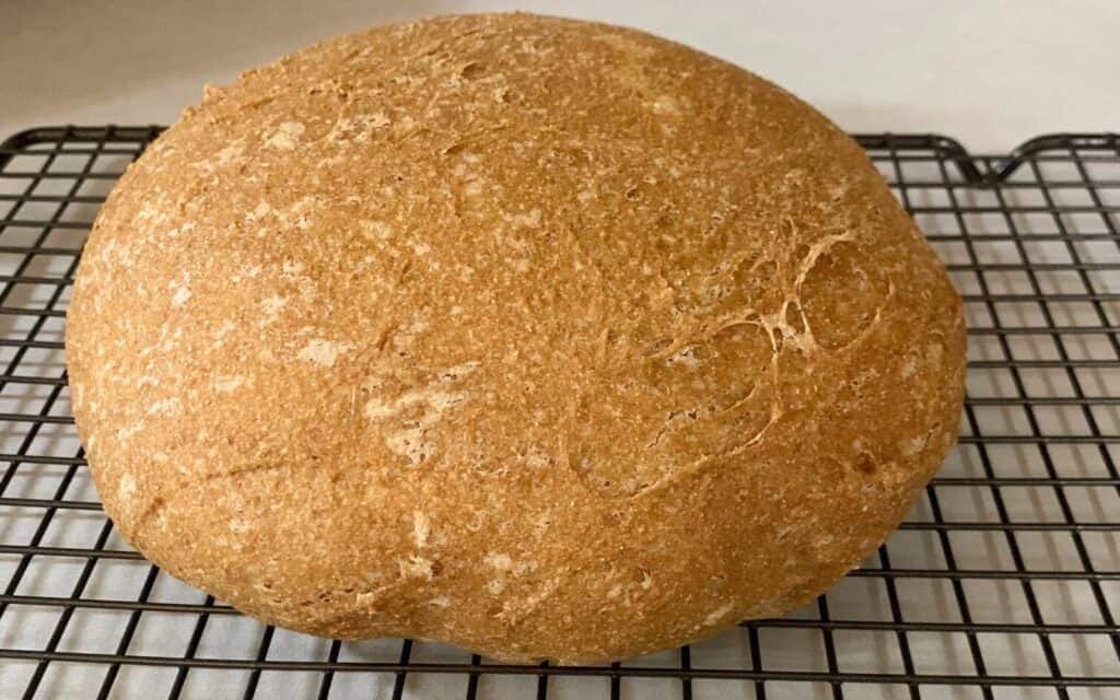 A fresh loaf of homemade whole wheat bread on a cooling rack on a kitchen counter.