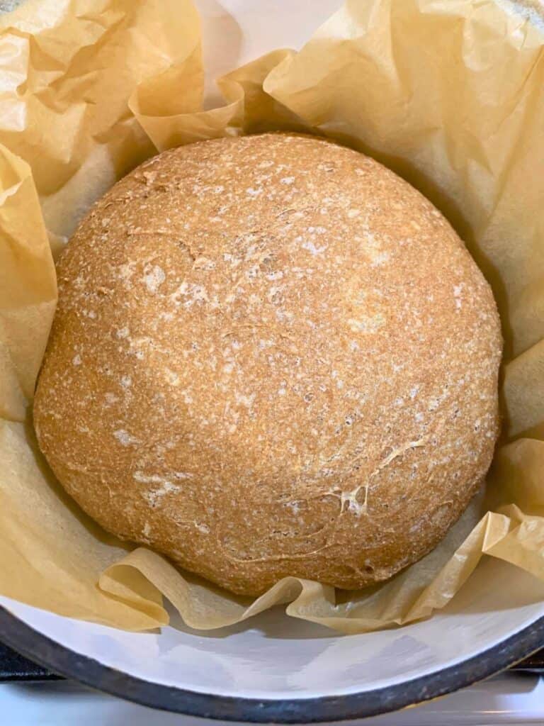 A loaf of homemade bread inside a Dutch oven lined with parchment paper.