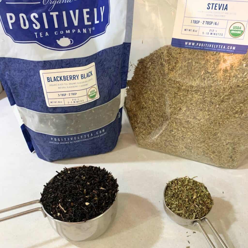 Ingredients for making blackberry tea including dried stevia leaves and dried blackberry tea leaves in stainless steel measuring cups on the counter.