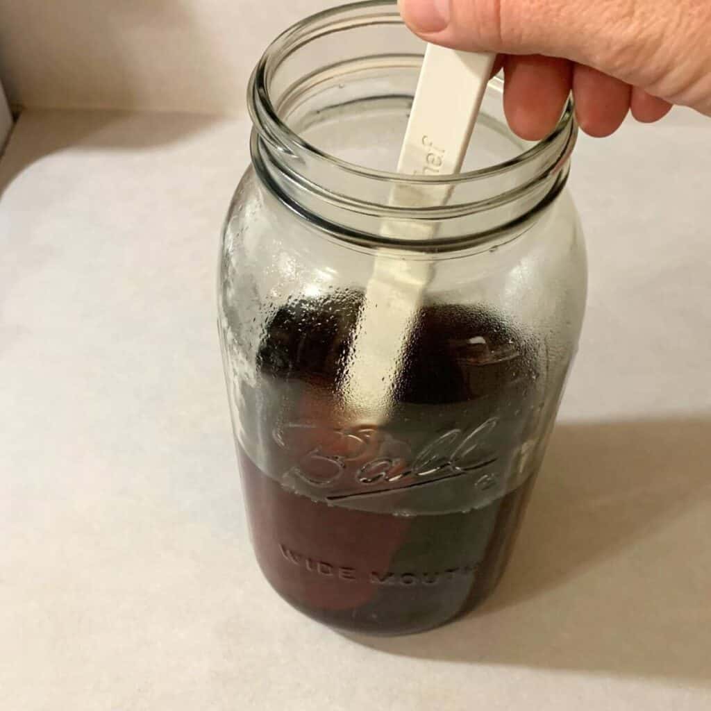 Woman stirring blackberry tea and sugar in a half gallon glass mason jar to dissolve the sugar.