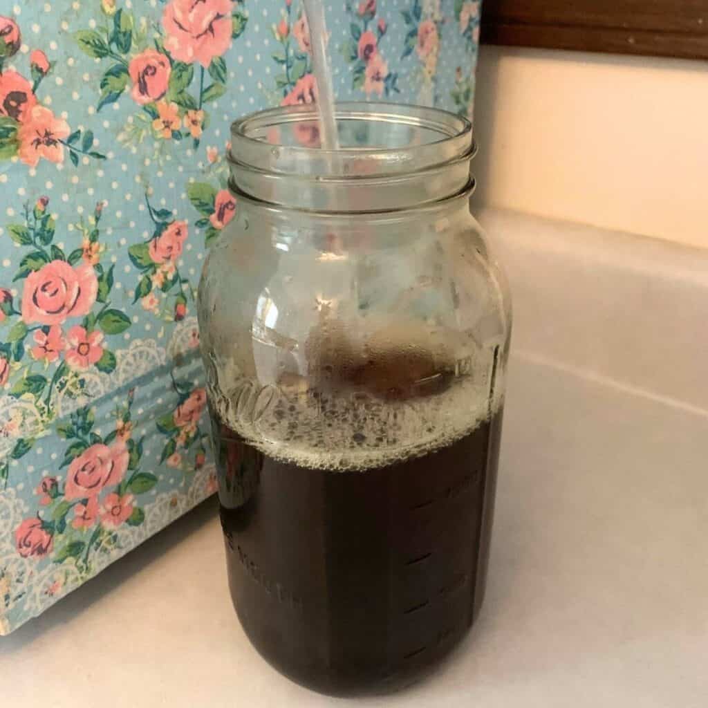 Woman adding water to top off blackberry tea in a glass jar.