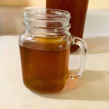 A glass mason jar of organic blackberry tea sitting on a kitchen counter in front of a half-gallon mason jar of blackberry tea.