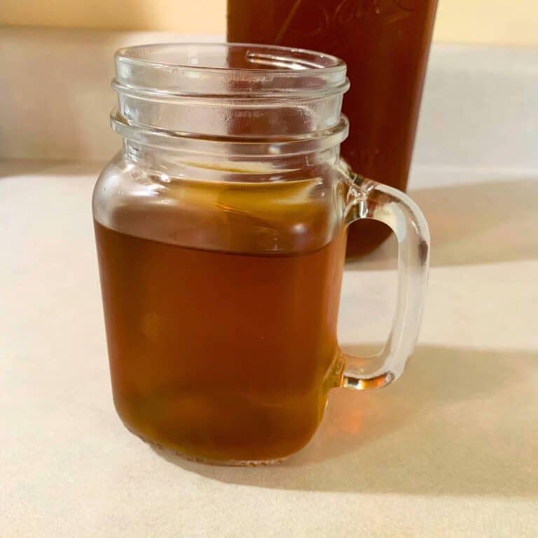 A glass mason jar of organic blackberry tea sitting on a kitchen counter in front of a half-gallon mason jar of blackberry tea.