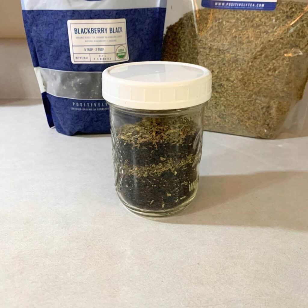 A glass pint jar of blackberry tea and stevia leaves sitting on the counter in front of bulk bags of dried blackberry tea and stevia leaves.