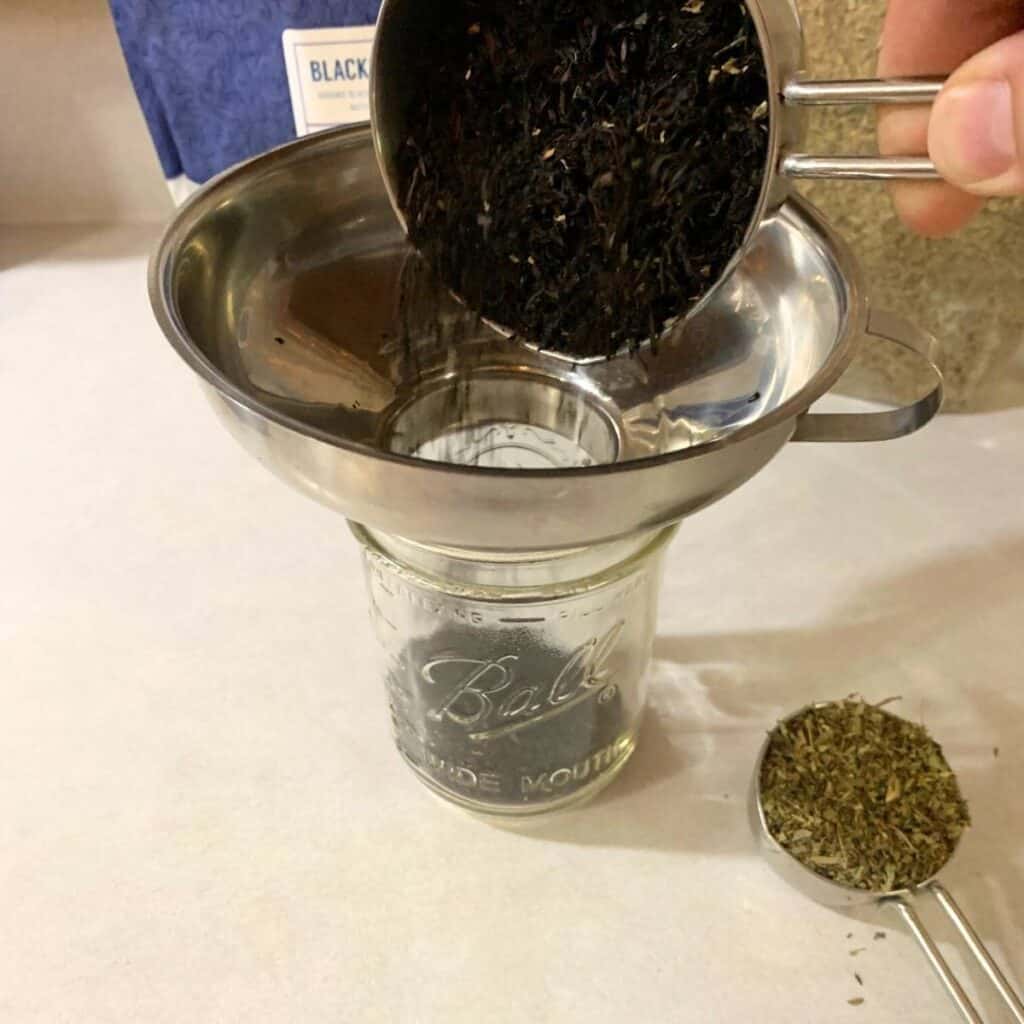 Woman adding blackberry tea leaves and stevia leaves to a pint mason jar.