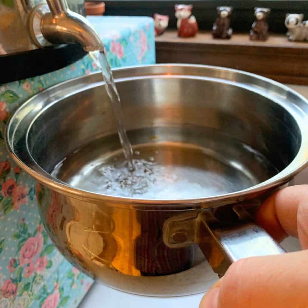 Woman adding water to a stainless steel pot.