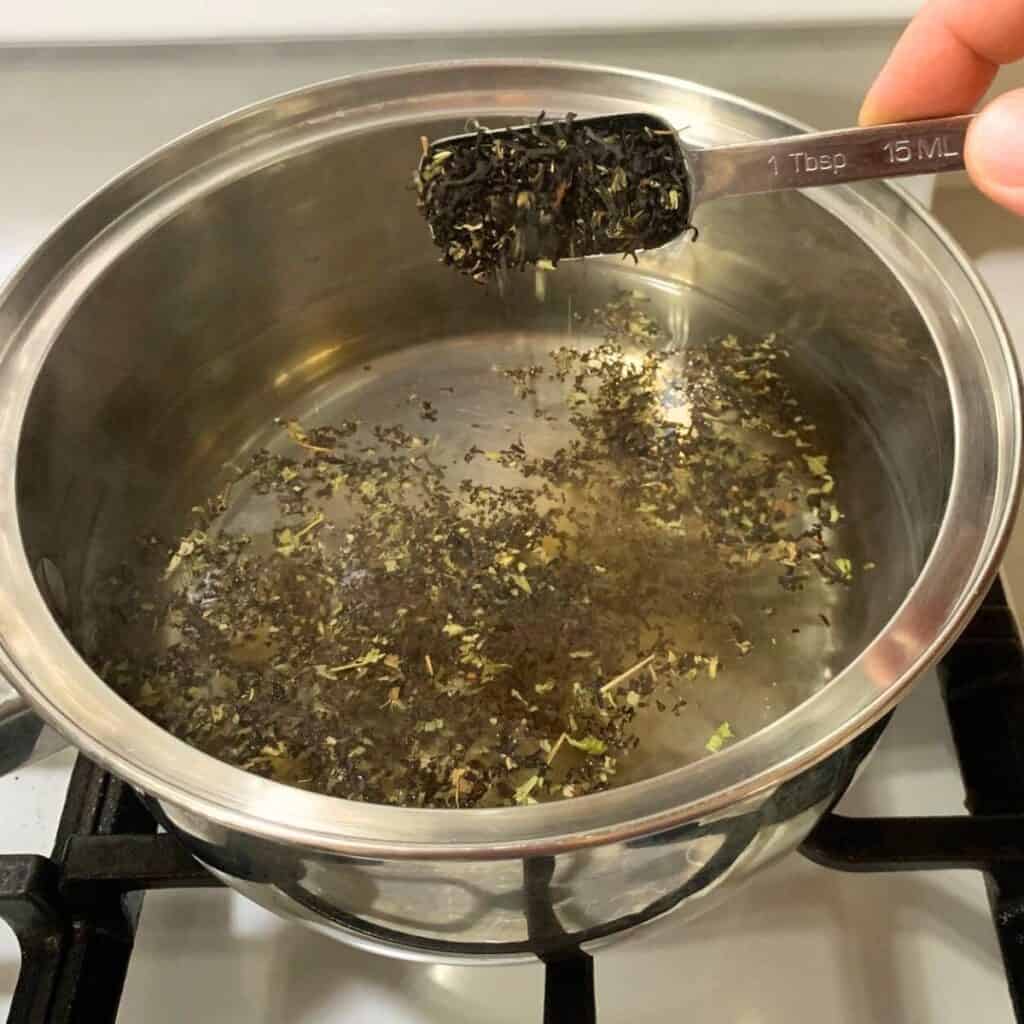 Woman adding blackberry tea to a stainless steel pot with water in it.