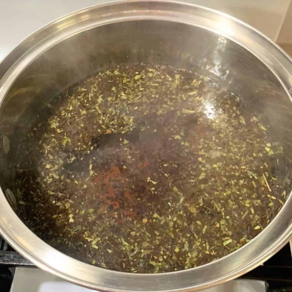 Loose leaf blackberry tea in a stainless steel pot with water in it.