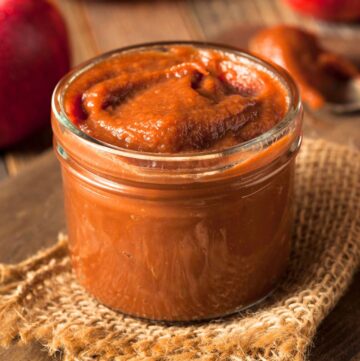 A glass jar of apple butter sitting on a burlap napkin.