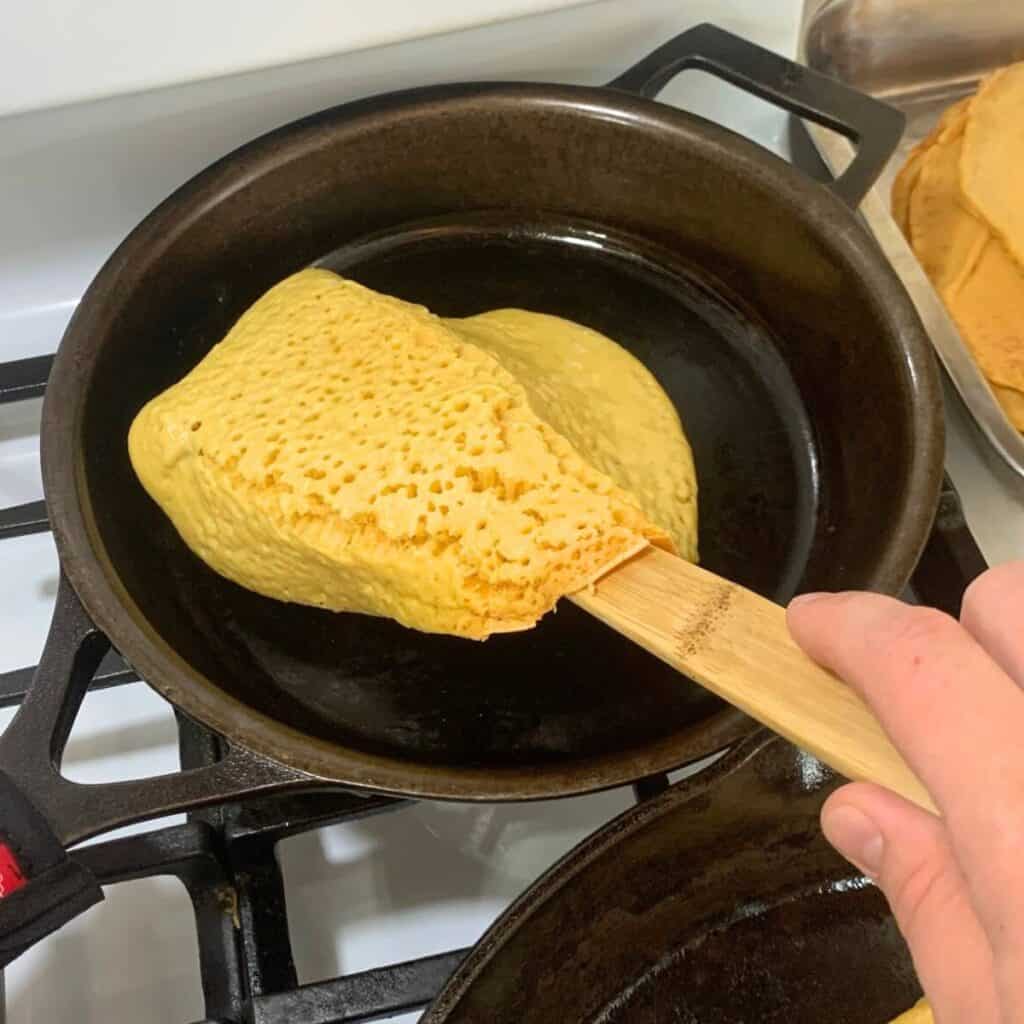 Woman flipping over a pancake in a cast iron skillet.