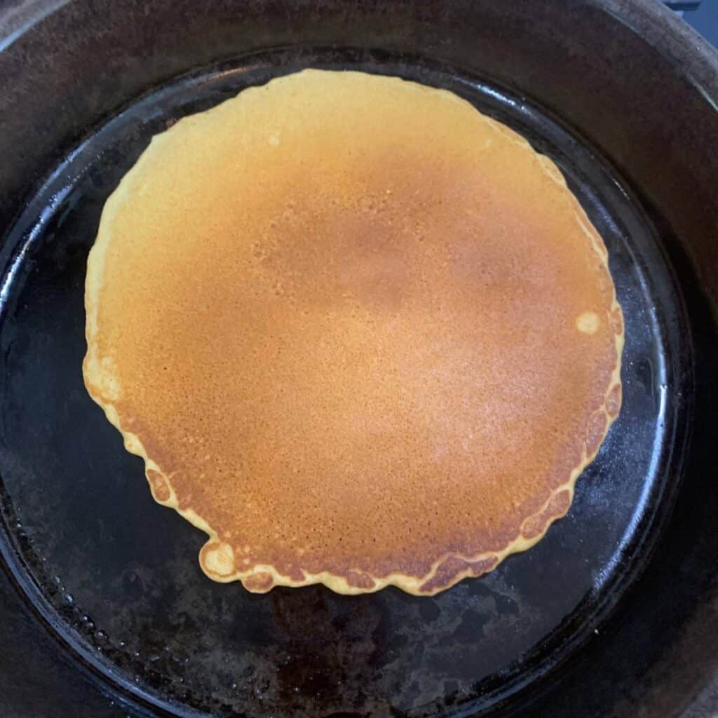 A pancake cooking in a cast iron skillet.