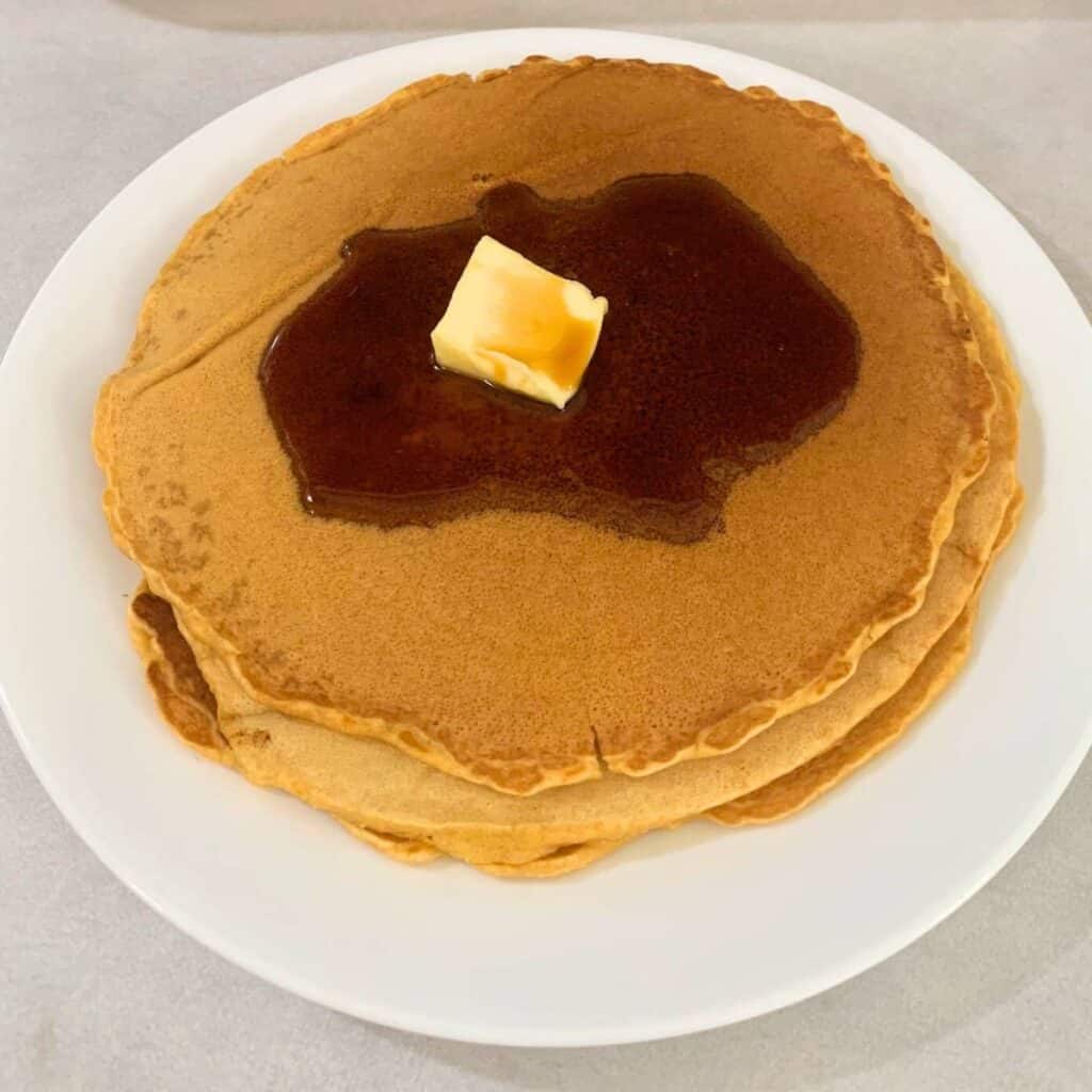 Pancakes on a white plate with butter and maple syrup melting on top.