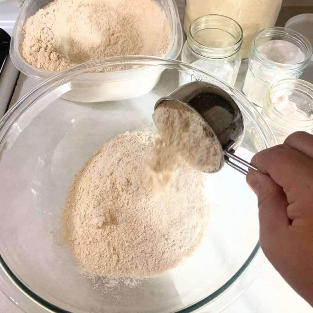 Woman adding freshly milled flour to a large glass mixing bowl.