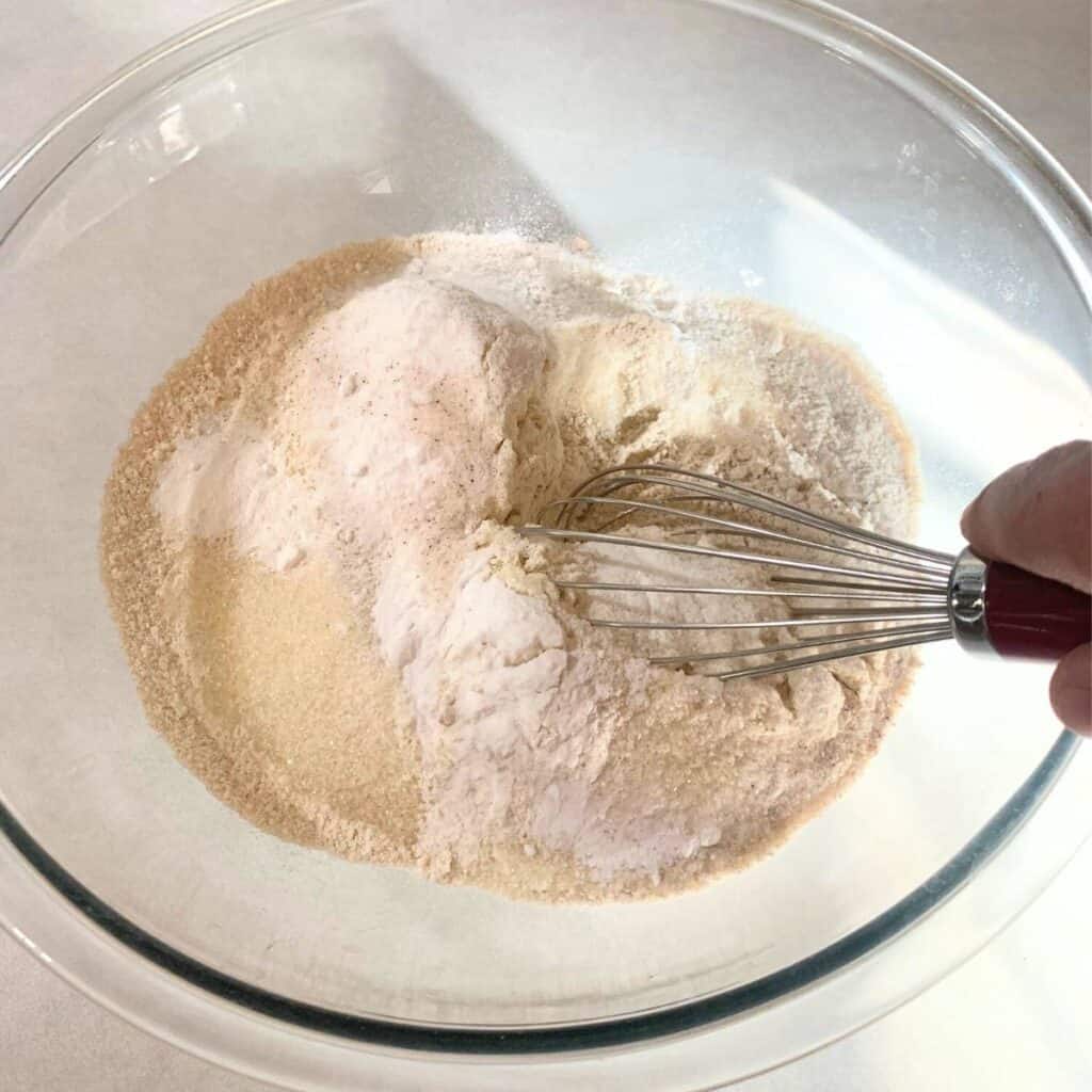 Woman mixing dry ingredients in a large glass bowl and making a well in the center.