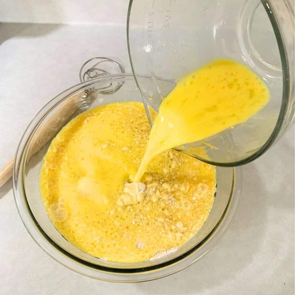 Woman pouring wet ingredients into the bowl with the dry pancake ingredients.