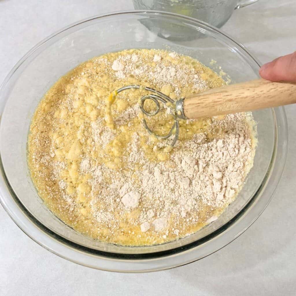 Woman using a dough whisk to combine the wet and dry ingredients for the best homemade pancakes using freshly milled flour.