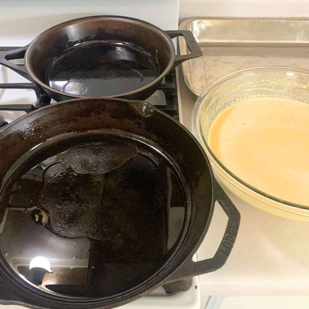 Cast iron skillets on top of a gas stove next to a large bowl of pancake batter.