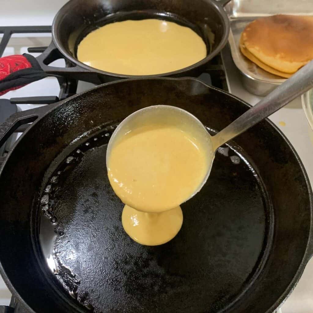 Woman adding a ladle full of pancake batter to cast iron skillets.