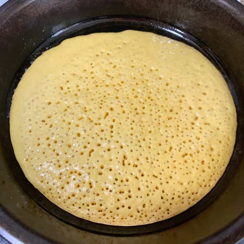 A large pancake cooking in a cast iron skillet.