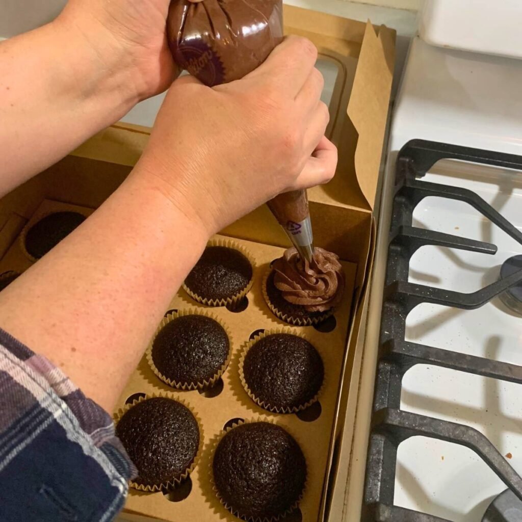 Woman piping chocolate icing onto chocolate cupcakes.