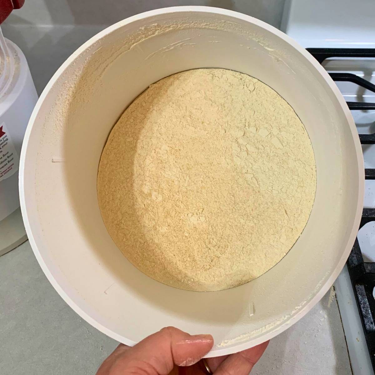 A woman holding a white tub of freshly milled wheat flour.