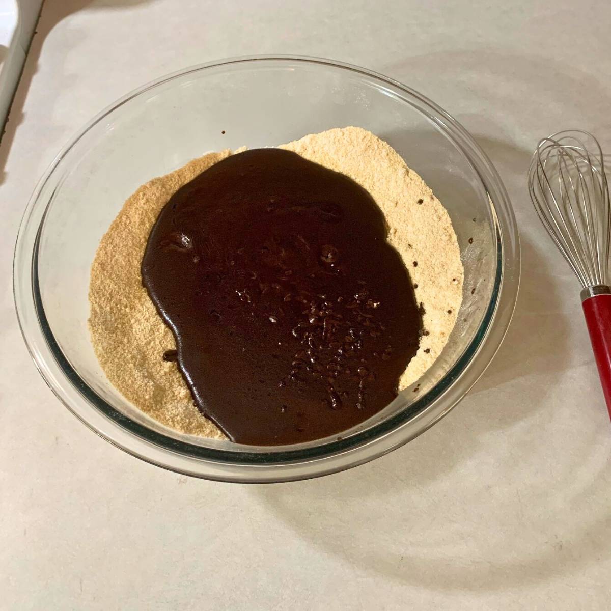 A glass bowl with sugar, freshly milled flour, and chocolate mixture poured inside.