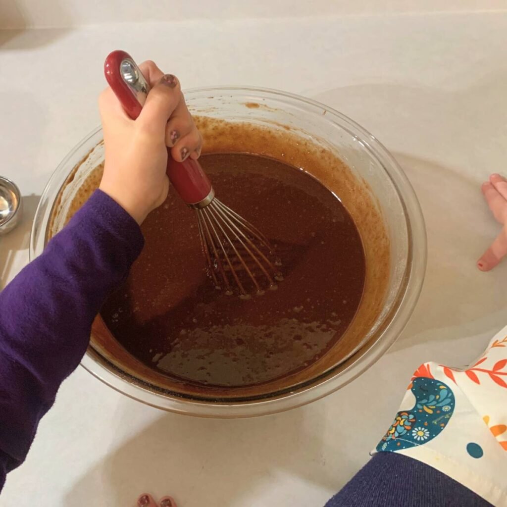 Little girl stirring chocolate cupcake batter in a glass bowl.