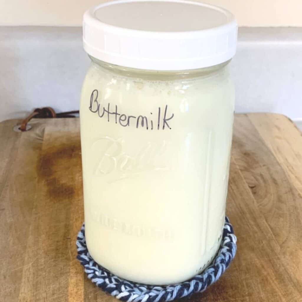 A quart jar of homemade buttermilk sitting on a blue coaster and wood cutting board.