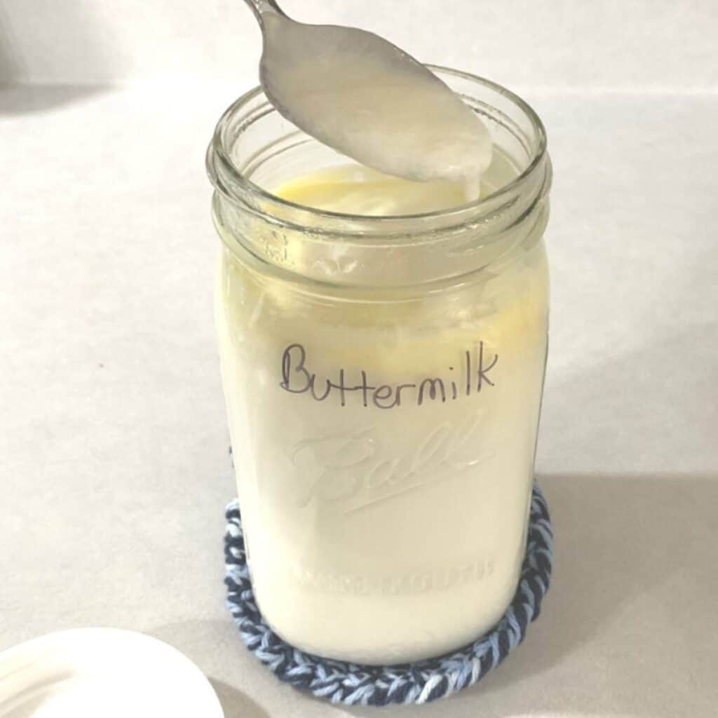 Woman stirring buttermilk in a quart mason jar.