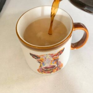 Woman adding hot coffee to a mug with sugar, vanilla bean extract, and heavy cream.