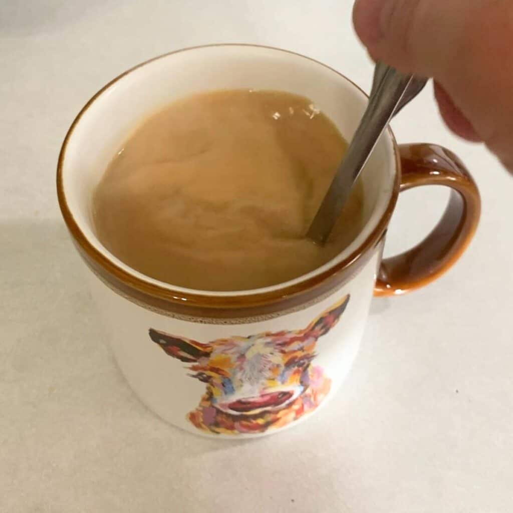 Woman stirring hot coffee with sugar, cream, and vanilla extract.