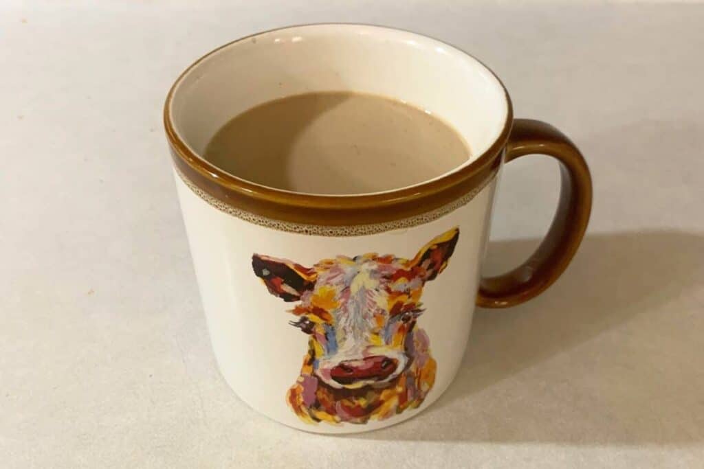 A coffee mug full of hot vanilla coffee sitting on a counter. The coffee mug has a picture of a cow on it.